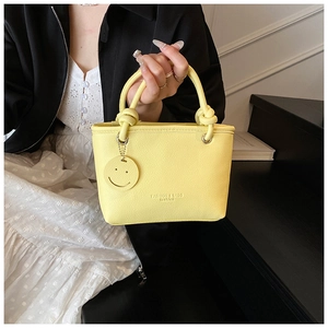 Detailed shot of yellow PU tote bag with smiley pendant and knotted handle accents