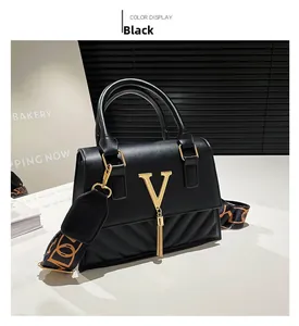 Detail of black leather handbag with gold V-logo, tassel charm, and patterned strap