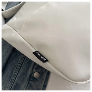 Close-up of white crossbody bag with FANYISSA woven label detail and smooth finish