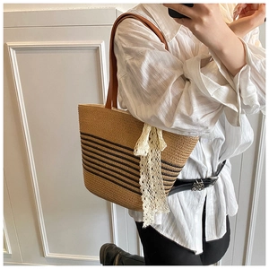 Detail of hand-woven straw tote bag featuring black stripes and white lace ribbon detail