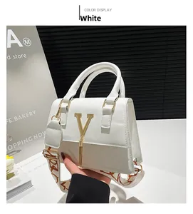 Close-up of white leather handbag with gold V-shaped buckle, long fringe and wide strap