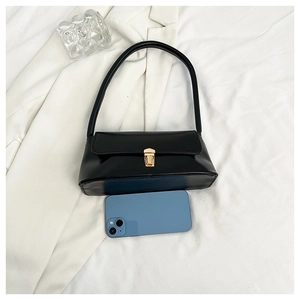 Detail of black glossy shoulder bag with gold clasp shown next to a smartphone for scale