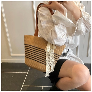 Detail of hand-woven straw tote with black stripes and elegant lace bow accessory