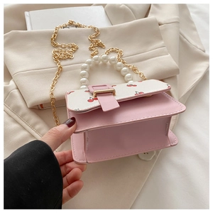 Detail of pink small flap bag with cherry print, faux pearl handle and gold chain strap