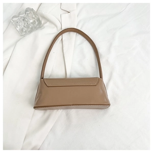 Flat lay of brown leather baguette bag on white blazer with glass cup in soft lighting