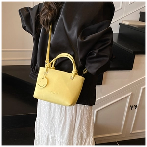Detail of yellow lychee leather bucket bag with fashion print and smiley charm