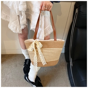 Close-up of woven straw tote bag featuring brown leather handles and a white lace bow