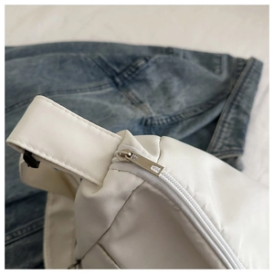 Close-up of silver metal zipper and stitching detail on a white canvas crossbody bag