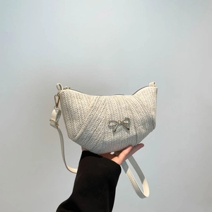 Chic beige woven crescent bag with metal bow detail and adjustable shoulder strap