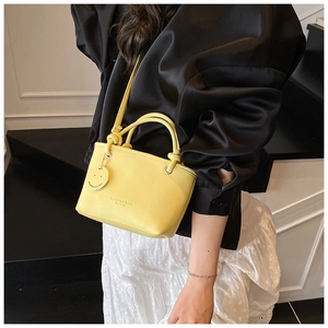 Chic bright yellow lychee leather handbag with a smiley charm on a minimal staircase backdrop