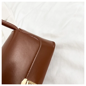 Detail of dark brown leather shoulder bag featuring golden clasp and reinforced stitching