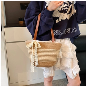 Detail of woven straw bucket bag featuring leather handles and white lace bow decoration