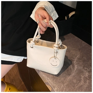 Detail of lychee textured cream bucket bag featuring knotted handles and a smiley pendant