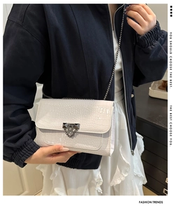 Detail of white crocodile texture on a stylish crossbody bag with silver metal chain strap