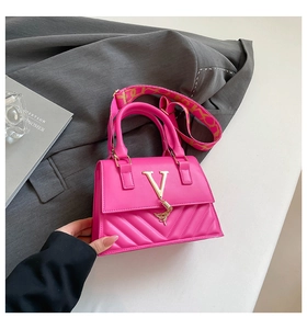 Detail of magenta square handbag featuring gold V logo and patterned wide shoulder strap