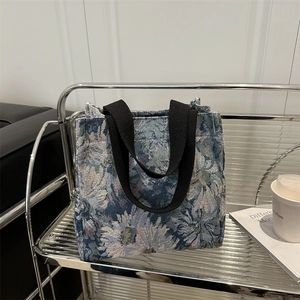 Blue floral jacquard tote bag with black handles on a modern minimalist metal shelf