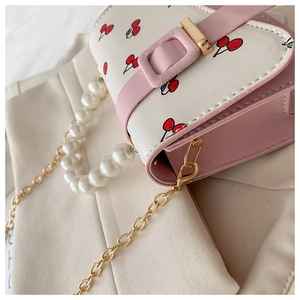 Detail of white cherry print square handbag featuring large pearl handle and pink trim