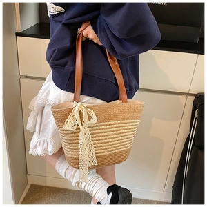 Close-up of a striped straw tote bag featuring a large lace bow and leather handles