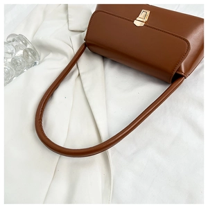 Detail of a brown leather underarm bag featuring a trapezoid gold twist lock and fine texture