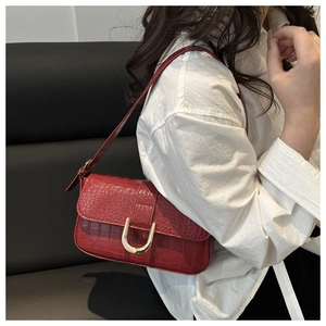 Close-up of red crocodile embossed leather shoulder bag with gold U-shaped buckle detail
