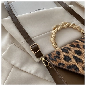Detail of leopard print flap and golden twisted metal handle on a brown crossbody bag