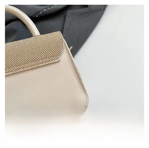 Dettaglio della borsa in pelle beige con patta in trama dorata e attacco manico metallico