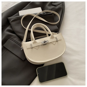Détail d'un sac selle crème avec fermoir rotatif argenté sur fond de costume gris élégant