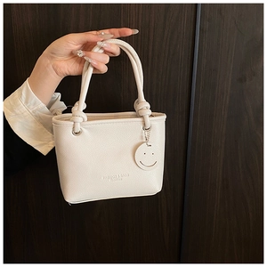 Close-up of beige lychee grain bucket bag with knot handles and smiling face pendant