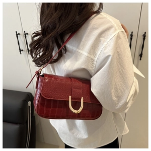 Detail of dark red crocodile pattern bag with gold U-buckle worn on shoulder
