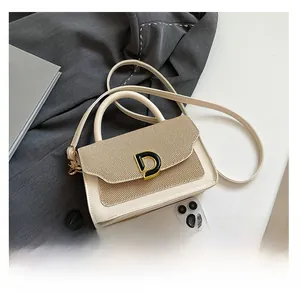 Dettaglio borsa beige intrecciata con fibbia a D dorata, accanto a smartphone per scala