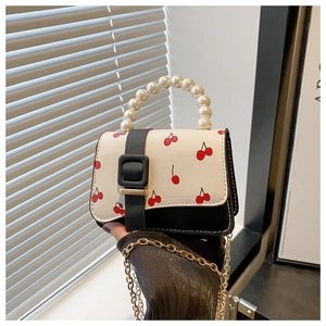 Detail of mini crossbody bag with pearl handle and vibrant red cherry prints