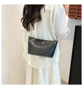 Détail d'un sac seau noir à motif litchi porté par un mannequin avec bandoulière