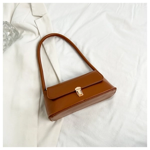 Detail of caramel faux leather shoulder bag with elegant gold metal buckle on white fabric