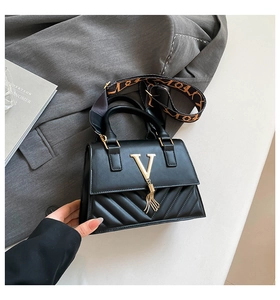 Detail of black crossbody bag with gold V logo, fringe tassel, and wide patterned shoulder strap