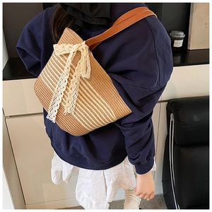 Detail of hand-woven straw bag with white lace bow and brown leather strap