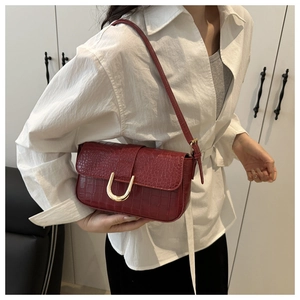 Detail of burgundy crocodile-embossed leather shoulder bag with gold U-shaped buckle