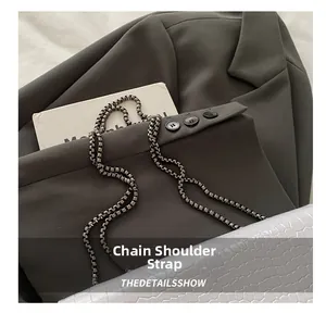 Close-up of industrial silver metal square box chain strap on stone textured leather bag
