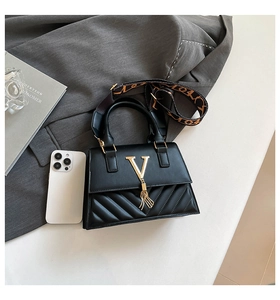 Detail of black quilted crossbody bag with gold V-logo and vintage floral strap
