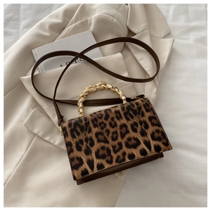 Detail view of leopard print crossbody bag with gold woven handle on elegant suit