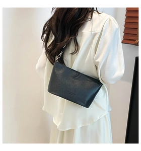 Gros plan du sac seau noir en cuir grainé avec logo embossé sur l'épaule du mannequin