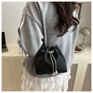 Détail du sac seau plissé noir avec chaîne argentée et perles porté par un mannequin