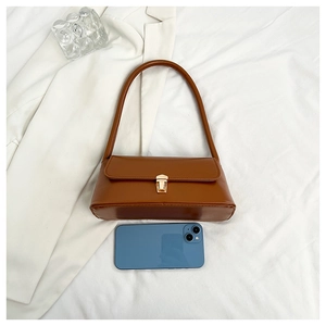 Close-up of brown leather baguette bag with gold buckle on white fabric background