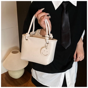 Detail of cream white leather bucket bag with rope handle and smiley face charm