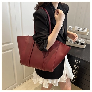 Deep burgundy leather bucket bag shown as a shoulder bag on a stylish female model