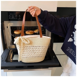 Detail of straw woven tote bag with brown leather handles and decorative white lace bow