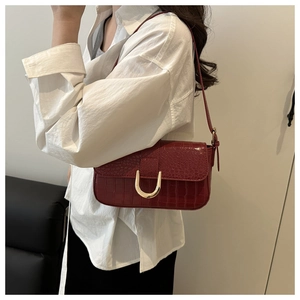 Detailed close-up of dark red crocodile embossed shoulder bag with gold horseshoe buckle