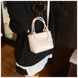 Detail of cream PU leather handbag featuring knotted handle and smiley face pendant charm