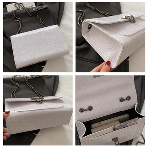Detail view of white croc-embossed bag showing metal chain, lock and internal storage