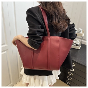 Burgundy leather tote bag with long straps shown on shoulder in a modern office setting