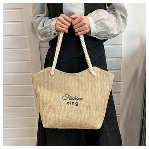 Close-up of woven straw tote bag featuring rope handles and Fashion xing embroidery